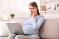 Anxious Pregnant Lady With Laptop Browsing Internet Sitting On Sofa