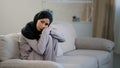 Anxious sad young woman in black hijab sitting on couch in living room suffering from psychological problem trouble at Royalty Free Stock Photo