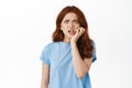 Anxious and scared redhead woman biting fingers and looking frightened, staring at camera with nervous face, fear of