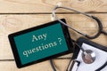 Any questions ? - Workplace of a doctor. Tablet, stethoscope, clipboard on wooden desk background. Top view Royalty Free Stock Photo