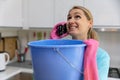 Apartment flooded by upstairs - worried woman calling repair service while water leaking from ceiling in bucket Royalty Free Stock Photo