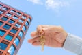 Apartment key in a man`s hand. Brass house door lock key. Modern building, view from below. Architecture in modern city. Royalty Free Stock Photo