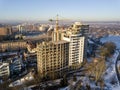 Apartment or office tall building under construction, aerial view. Tower crane silhouette Snowy field and distant city on bright