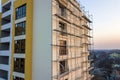 Apartment or office tall unfinished building under construction. Brick wall in scaffolding, shiny windows and tower crane on urban Royalty Free Stock Photo