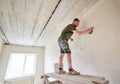 Apartment remodel. Worker is standing on wooden stand and puttying the walls indoors at small room Royalty Free Stock Photo