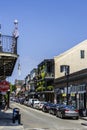 Apartments with balconies along a street with parked cars in the French quarters, with lush green plants, people walking