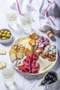 Aperitif, champagne and snack of sausage, cheese, nuts, olives and crackers on a light background.