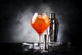 Aperol spritz cocktail in big wine glass with orange and ice, summer alcoholic cold drink, dark bar counter with steel bar tools,