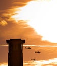 Three apache helicopters flying past a tower with clouds