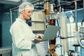 Apothecary scientist working with laptop near CBD oil extractor in laboratory.