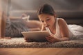 An app a day keeps boredom away. an adorable little girl using a digital tablet on the floor at home with her mother in Royalty Free Stock Photo