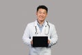 App for health care remote. Smiling korean chinese male therapist in white coat with stethoscope shows tablet