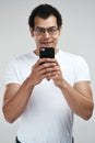 This app will make me tons of money. a handsome young man using his cellphone while standing against a grey background. Royalty Free Stock Photo