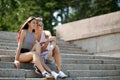 A sweet pair of beautiful girl with an attractive fellow seating on steps on a natural blurred background.