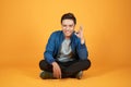 Appealing young Asian man sitting with his legs crossed and showing okay sign. Isolated on orange background Royalty Free Stock Photo