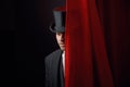 Appearing handsome man magician peeking out from behind stage drapery curtain Royalty Free Stock Photo