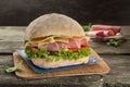 Appetising ciabatta sandvich with ham, cheese, tomato and green salad on the wooden background