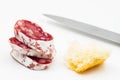 Appetizer of a piece of salami sausage, bread, and a knife isolated on a white background