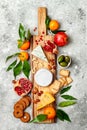 Appetizers table with antipasti snacks. Cheese variety board over grey concrete background. Top view, flat lay.