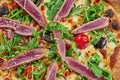 Appetizing baked pizza with tuna, arugula, cherry tomatoes and parmesan with crisp on a wooden background. Restaurant serving. Royalty Free Stock Photo