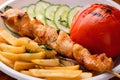 Appetizing chicken kebab, fried potatoes chips, grilled tomato and fresh sliced cucumbers close-up