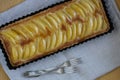 Appetizing freshly baked pear tart with whiskey icing for dessert for a date and two forks on a gray linen background.