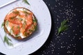 Appetizing half of a bun with smoked fish, fresh cream, sprinkled with dill and sesame seeds, on a white plate