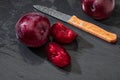 Appetizing and healthy red plums, whole and cut into segments with a rustic appearance on a black background