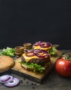 Appetizing homemade burgers with a juicy beef chop, red onion, cheese, salad and tomatoes, on vintage cutting board, close up,