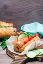 Appetizing hot dog made from fried sausage, rolls and fresh vegetables, wrapped in parchment paper on a cutting board Royalty Free Stock Photo