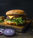 Appetizing juicy home burger with beef, salad, pickled cucumbers, cheese and onion, bun with sesame, on a vintage cutting board