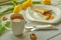 Appetizing pancakes with fruit jam, a cup of tea with lemon, yellow tulips, fork and knife Royalty Free Stock Photo