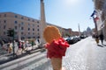 Appetizing pink berry ice cream in waffle cone in female hand over Rome city view. Tasty ice cream like a symbol of summer