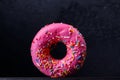 Appetizing pink donut with scattering on a black background