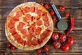 Appetizing pizza with pepperoni and salami lies on a wooden surface next to beautiful tomatoes and red pepper. Picnic and barbecue Royalty Free Stock Photo