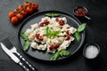 Appetizing ravioli with tomato sauce cheese and basil with basil parmesan and tomatoe on black plate on black background