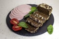 Appetizing sausage bologne sliced on a slate board on a light marble background with tomatoes and basil close up