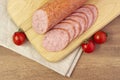 Appetizing sausage sliced on a yellow plate on a rough linen background with chilli pepers and spices close up
