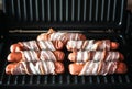 Appetizing sausages wrapped in bacon are grilled on a electric grill Royalty Free Stock Photo
