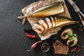 Appetizing smoked fish with spices, cutlery, pepper and bread on craft paper over dark stone background. Sandwich with smoked Royalty Free Stock Photo