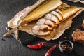 Appetizing smoked mackerel fish with spices, pepper and bread on craft paper over dark stone background. Mediterranean food,