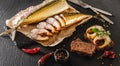 Appetizing smoked mackerel fish with spices, pepper and bread on craft paper over dark stone background. Mediterranean food, Royalty Free Stock Photo