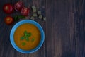Appetizing soup puree in a blue deep plate, tomatoes and slices of dried bread on a dark wooden background Royalty Free Stock Photo
