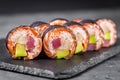 Appetizing sushi roll with tuna salmon escolar crab and avocado on a black stone plate