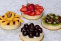 Appetizing tartlets with various berrys and fruits are lying on a white tablecloth. Royalty Free Stock Photo