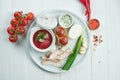 Appetizing Ukrainian borsch in a white bowl served with sour cream, lard, onions, garlic and bread on a white wooden background.