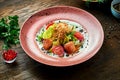 Appetizing warm salad with baked salmon, cherry tomatoes, lemongrass and white sauce, served in a white plate on a wooden