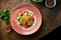 Appetizing warm salad with baked salmon, cherry tomatoes, lemongrass and white sauce, served in a white plate on a wooden