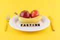 Apple, a banana and a tomato on a plate and the word 'fasting' written on wooden blocks Royalty Free Stock Photo