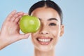 Apple, beauty and skin of a woman with a smile holding a fruit on her face against a blue studio background. Portrait of